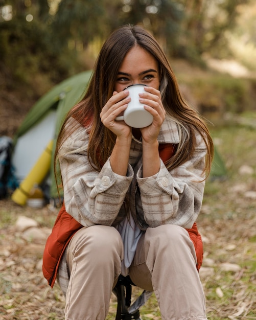 Foto gratuita ragazza di campeggio felice nella foresta che beve da una tazza