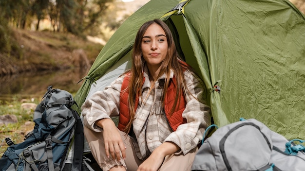テントの正面図に座っている森の中で幸せなキャンプの女の子