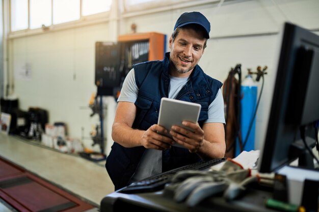 Happy car mechanic using digital tablet while working in auto repair shop