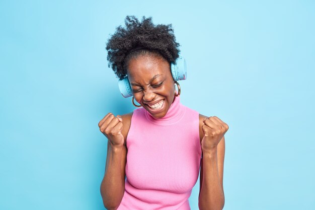 Happy carefree dark skinned female model makes yes gesture fist pump celebrates achievement of success 