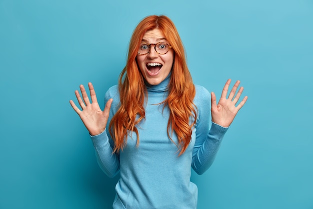 Happy carefree emotions. Excited redhead woman raises palms and looks gladfully screams with happiness dressed in casual clothes.