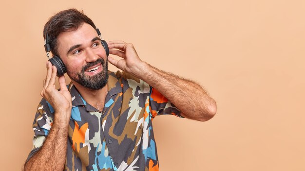 Happy carefree guy has thick beard listens music via wireless headphones