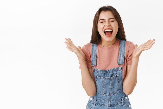 행복하고 평온한 젊은 여성이 환호하는 동안 웃고 눈을 감고 멋진 소식을 듣고 하늘에 대한 감사와 승리를 축하하는 기쁨이 우승자가 됩니다.