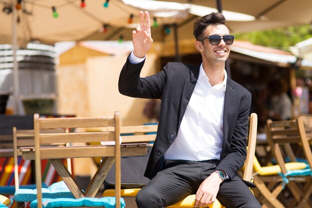 Happy carefree man waving with fingers to waiter