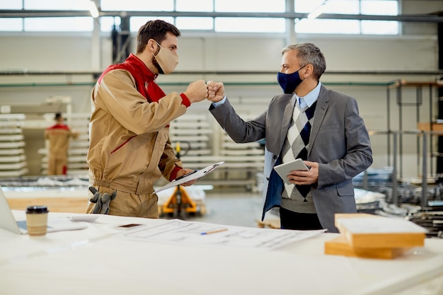 Happy carpenter fist bumping with inspector while greeting during coronavirus pandemic