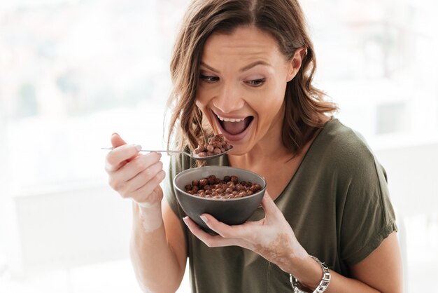 Happy casual woman eating from plate and looking away