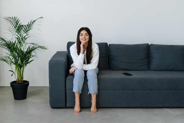 Free photo happy casual woman is talking on a phone sitting on a sofa at home