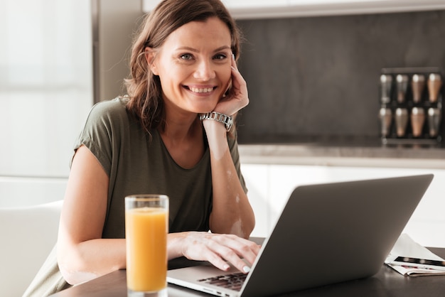 Happy casual woman sitting by the table with juice and tablet computer on kitchen