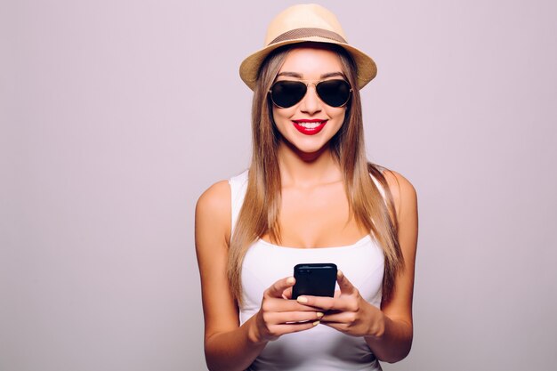 Счастливая случайная молодая женщина, использующая смартфон над серой стеной