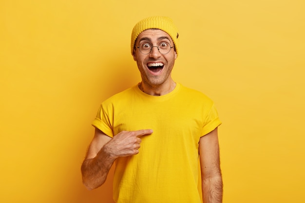 Free photo happy caucasian guy points happily at himself, has surprised joyful look, asks whether exactly he won competition