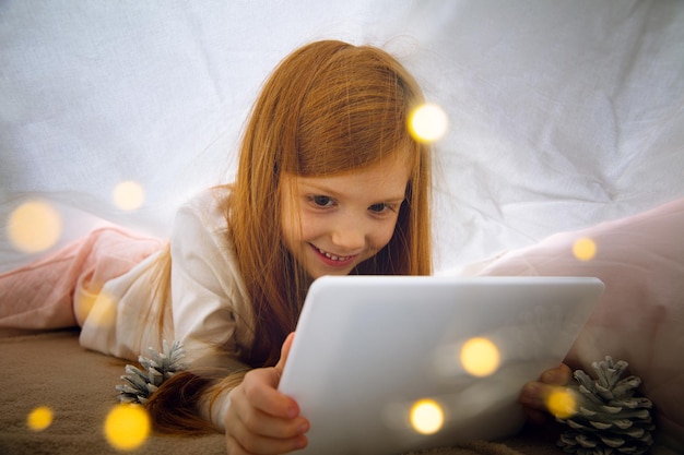 Happy caucasian little girl during video call or messaging with Santa using laptop and home devices