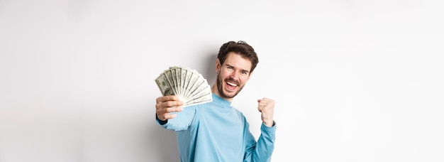 Бесплатное фото Счастливый кавказец протягивает руку с деньгами в долларах, говоря да и празднуя доход, получил cas
