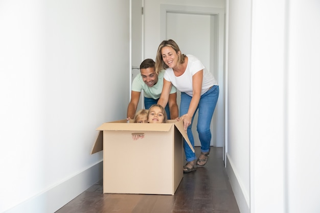 Happy Caucasian parents playing with children sitting in carton box at new home