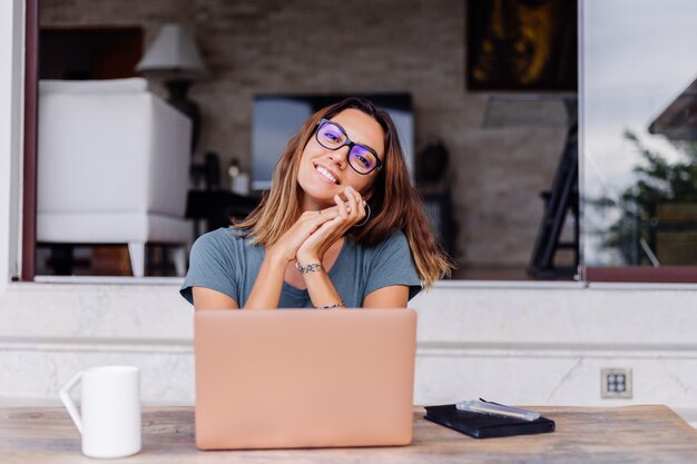 Happy caucasian woman does distance work on laptop at home comfortable place drinking tea