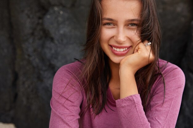 Happy Caucasian woman with pleased expression, looks joyfully , has green eyes, dark straight hair