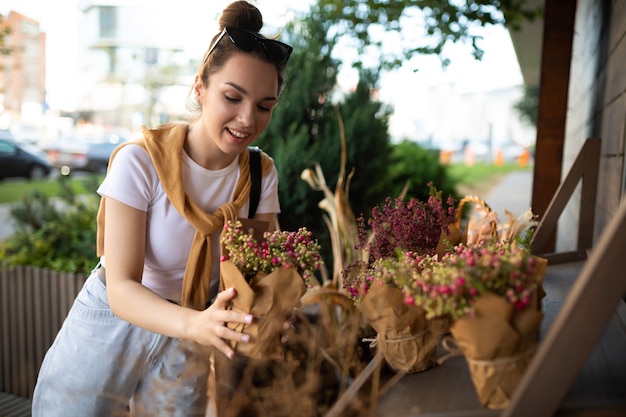 Happy caucasian young woman chooses potted flowers to buy at outdoor garden stall