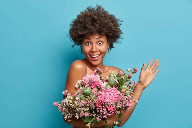 Free photo happy celebration concept. attractive fancy young lady holds bouquet of fowers raises palm looks with excited cheerful expression