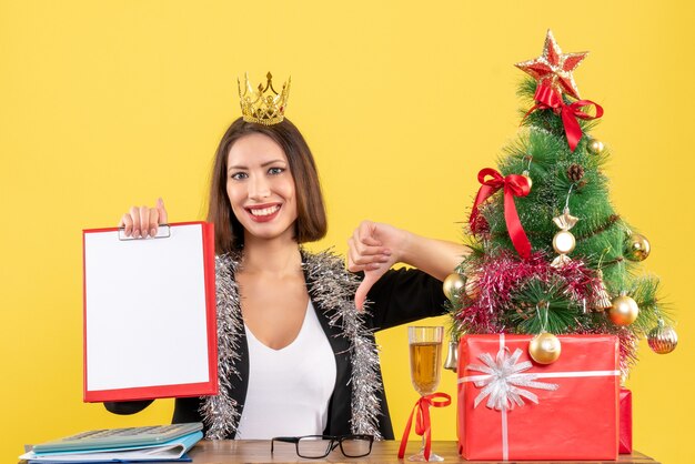 Happy charming lady in suit with crown holding document making negative gesture in the office 