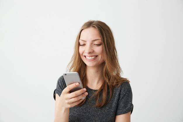 Happy cheerful girl smiling looking at phone screen typing text message .