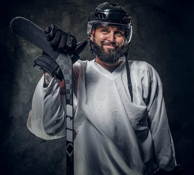 Happy cheerful hockey player has a photo session at dark photo studio.