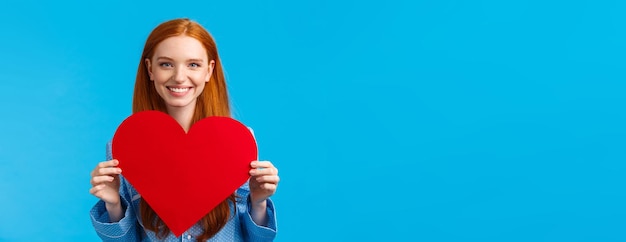 Happy cheerful and lovely tender caucasian woman holding big red heart valentines card and smiling g