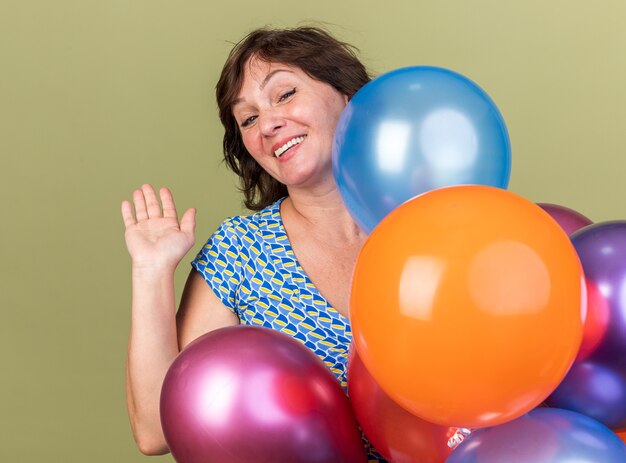 Счастливая и веселая женщина среднего возраста кучу разноцветных шаров, размахивая рукой, улыбаясь