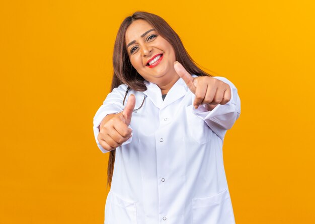 Happy and cheerful middle age woman doctor in white coat with stethoscope looking smiling showing thumbs up