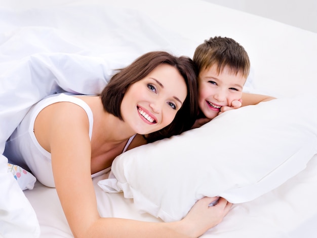 행복한 쾌활한 어머니와 그녀의 예쁜 아들이 침대에 누워