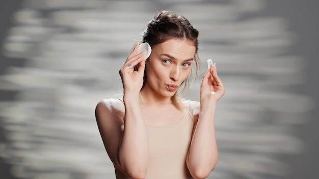 Happy cheerful person laughing with cotton pads on camera, using accessories to promote skincare routine and self confidence. young beautiful model acting positive and silly for ad.