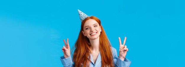 Happy cheerful redhead woman in birthday cap tilt head and smiling upbeat celebrating bday showing p