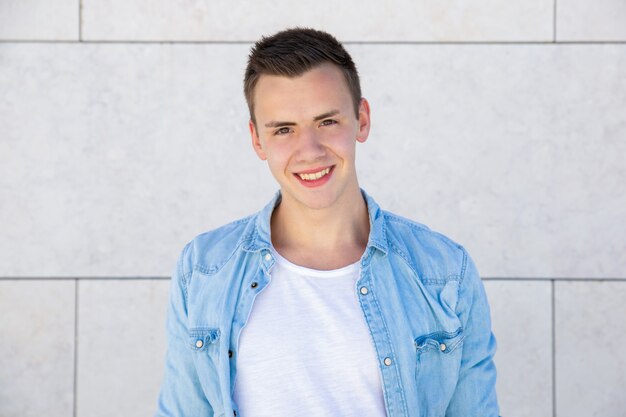 Happy cheerful student guy standing over pale outdoor wall