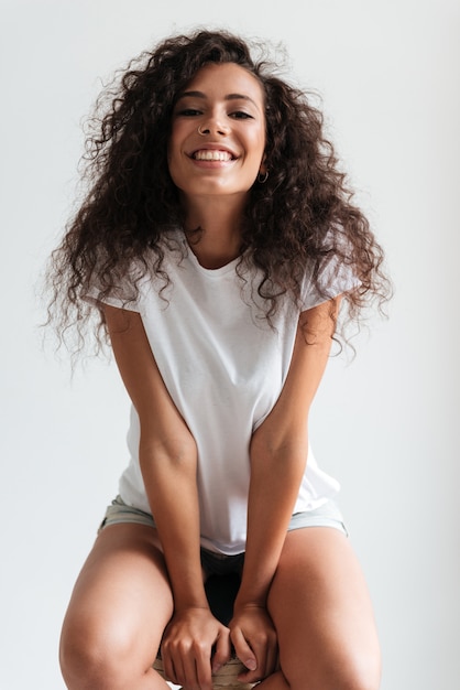 Foto gratuita donna allegra felice con capelli ricci che si siedono su una sedia