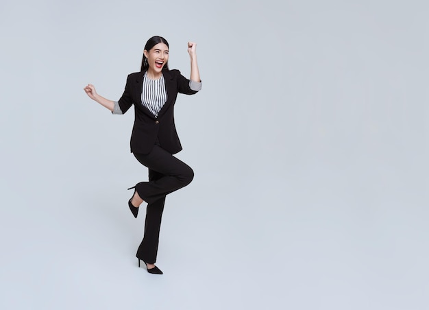 Счастливая веселая молодая азиатская деловая женщина в костюме прыгает в воздухе на белом фоне студии