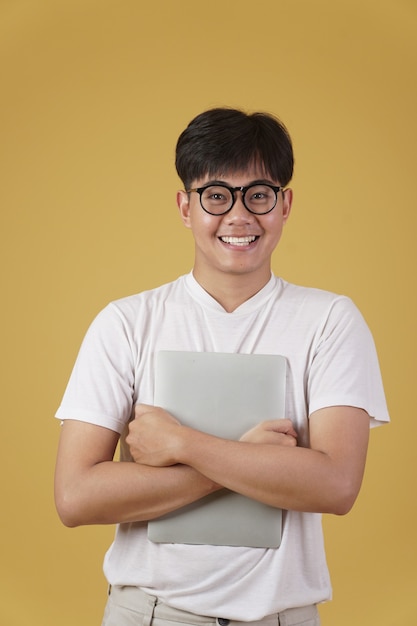 幸せな陽気な若いアジア人オタク学生は 分離されたラップトップコンピューターを保持している眼鏡を着てカジュアルに服を着て プレミアム写真