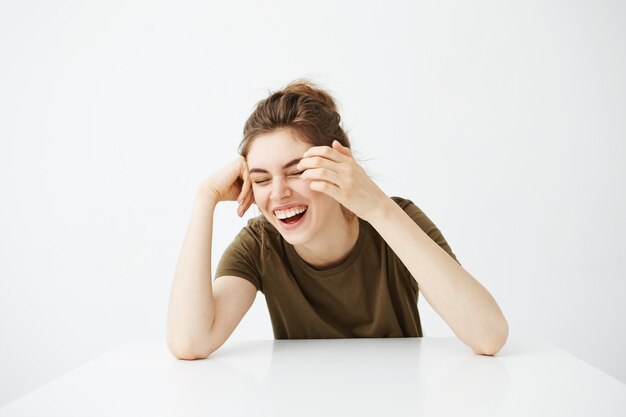 Happy cheerful young beautiful woman with bun smiling laughing sitting at table over white background.