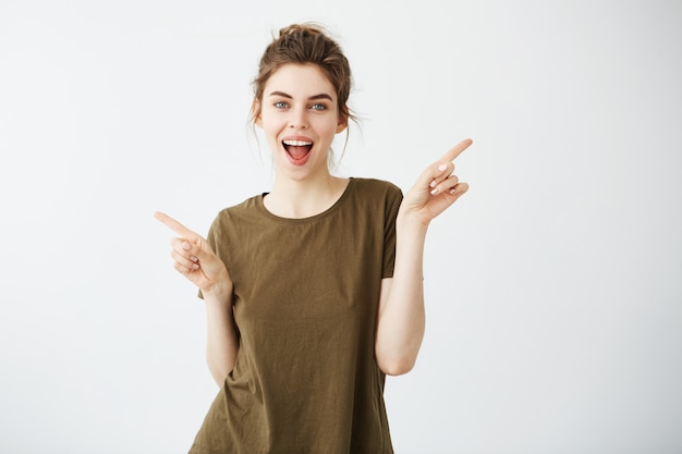 Happy cheerful young woman smiling with opened mouth pointing fingers in side.