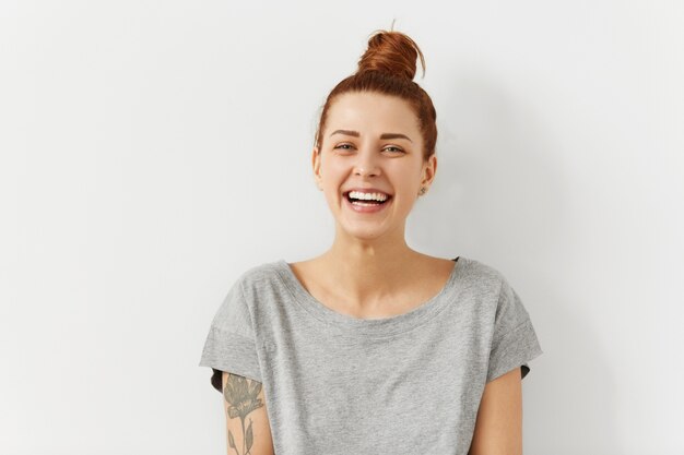 Happy cheerful young woman wearing her red hair in bun, looking joyful and charming smile