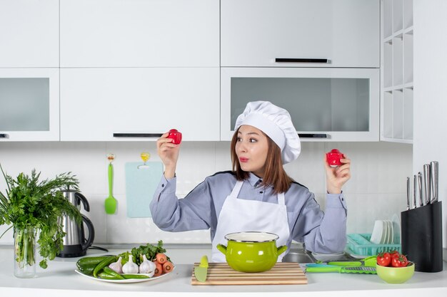 Happy chef and fresh vegetables with cooking equipment and holding tomatoes in the white kitchen