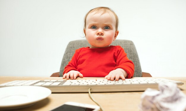 現代のコンピューターまたは白いスタジオで分離されたラップトップのキーボードで座っている幸せな子供女の赤ちゃん