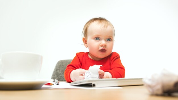 白いスタジオで隔離の現代のコンピューターまたはラップトップのキーボードで座っている幸せな子女の赤ちゃん