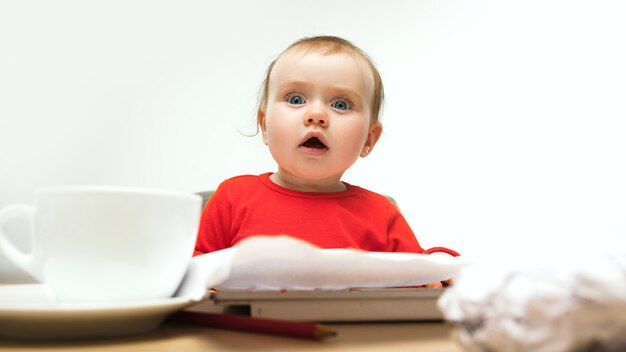 白いスタジオで現代のコンピューターやラップトップのキーボードで座っている幸せな子の女の赤ちゃん。