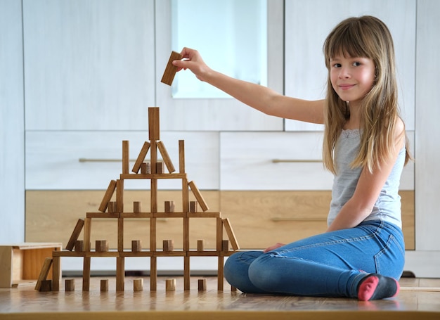 Happy child girl playing game stacking wooden toy blocks in high pile structure. hand movement control and building computational skills concept.