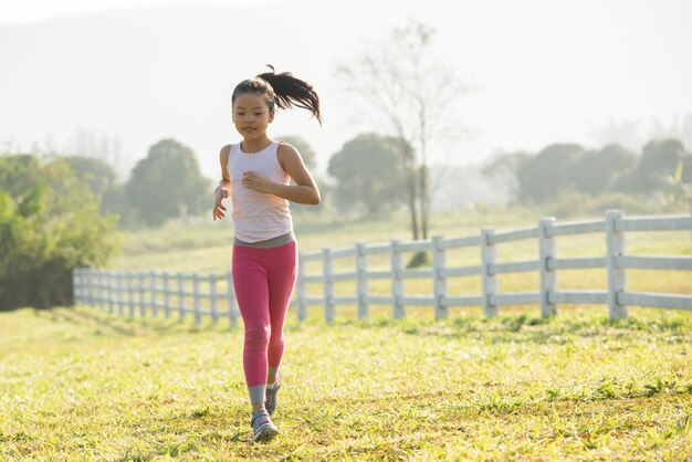 Ragazza felice del bambino che corre sul prato in estate in natura. bagliore di luce solare calda. il piccolo asiatico sta correndo in un parco. sport all'aria aperta e fitness, esercizio fisico e apprendimento della competizione per lo sviluppo del bambino.