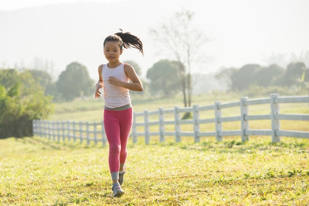 自然の中で夏の草原を走る幸せな子供の女の子。暖かい日差しのフレア。アジアのリトルが公園で走っている。子供の発達のためのアウトドアスポーツとフィットネス、運動と競技学習。