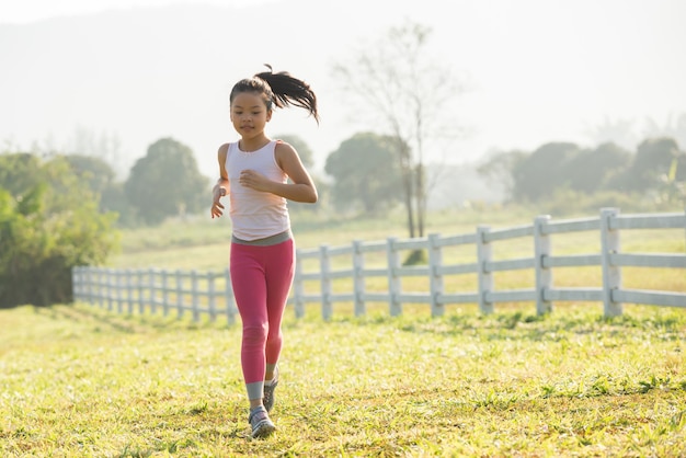 Happy child girl running on meadow in summer in nature. warm sunlight flare. asian little is running in a park. outdoor sports and fitness, exercise and competition learning for kid development.