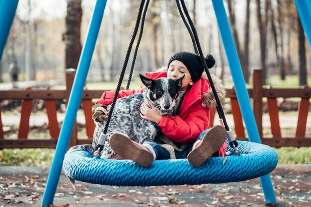 Happy child girl on swing. Little girl on a swing hugs her dog.