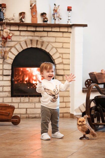 Счастливая маленькая девочка ребенка стоя дома против камина