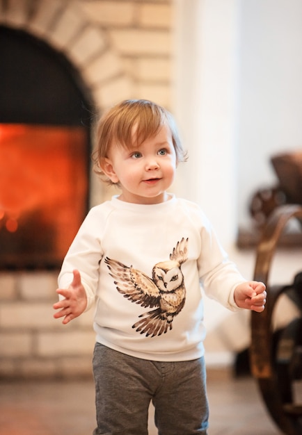 The happy child little girl standing at home against fireplace