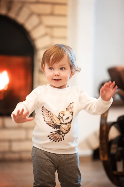 Free photo the happy child little girl standing at home against fireplace