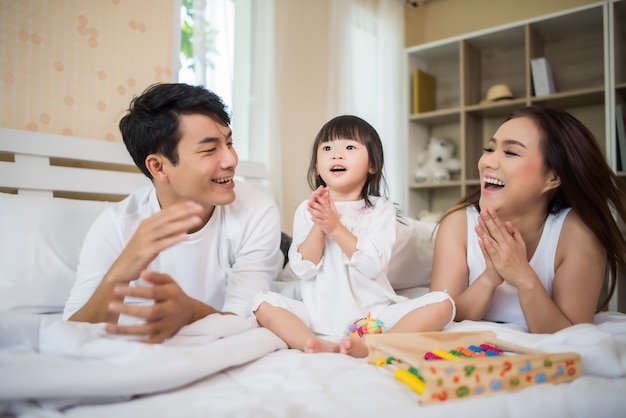 Счастливый ребенок с родителями, играющими в постели у себя дома